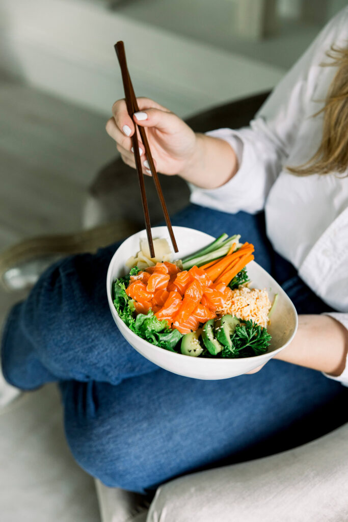A bowl of sushi and veggies in the hands of a person with chopsticks